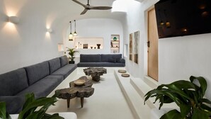 A modern living room with a grey sofa, a coffee table, and a ceiling fan. - Arithera Villa in Santorini (Santorini)