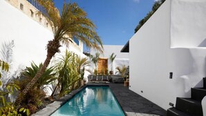 A pool area with a clear blue pool, surrounded by white walls and palm trees. - Arithera Villa in Santorini (Santorini)