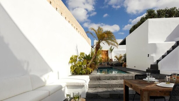 A modern outdoor patio with a pool, white walls, and a wooden table set for dining. - Arithera Villa in Santorini (Santorini)
