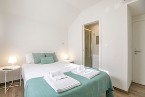 Een hotelkamer met een bed, twee nachtkastjes met lampen, een badkamedeur en een douchegedeelte.