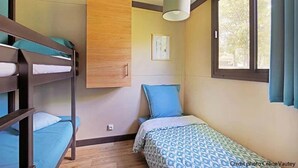 Een studentenkamer met stapelbedden, een enkel bed, een houten garderobe, een hanglamp en een raam met gordijnen.
