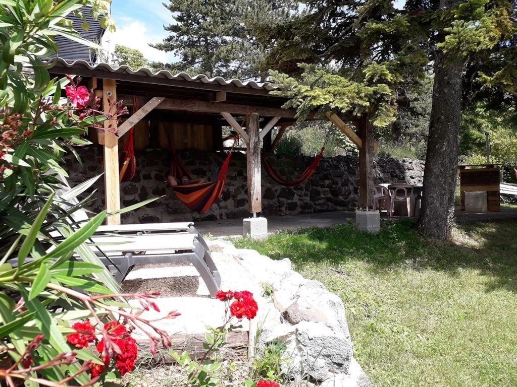 Un espace extérieur aménagé dans un style rustique, avec une pergola en bois, des murs en pierre et un hamac.