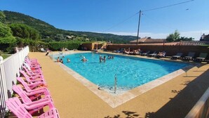 Una piscina con gente, rodeada de sillas de descanso y vistas a colinas.