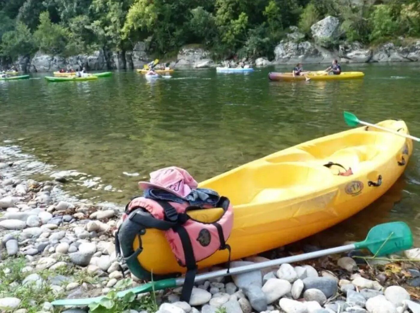 A yellow kayak with a pink bag and paddle on a rocky shore.