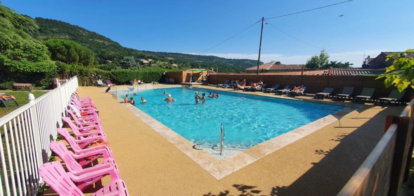 A swimming pool with people in it, surrounded by lounge chairs and a view of hills.