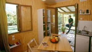 Cocina compacta con paredes de madera, una mesa de comedor y una cesta de frutas, y vista a zonas verdes al exterior.