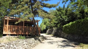 A wooden cabin with a balcony, surrounded by trees and a stone wall.