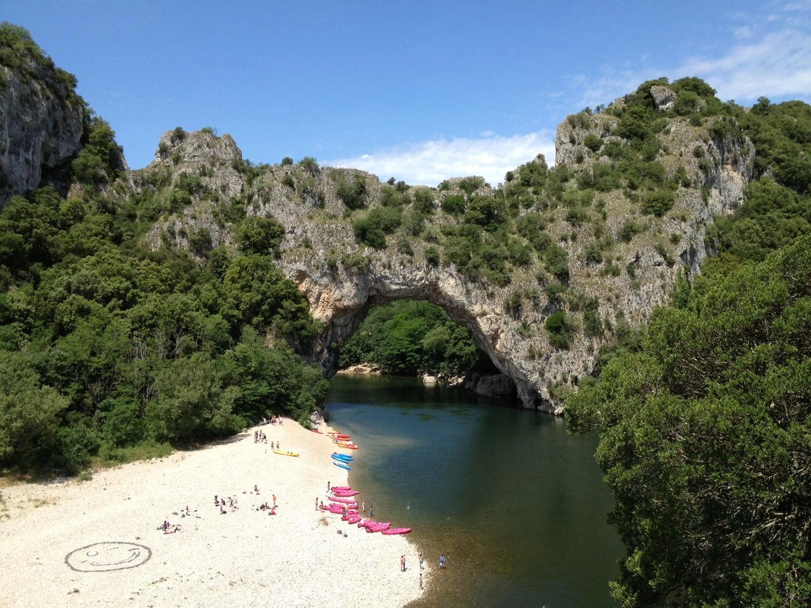 Una playa con un arco natural de roca, agua cristalina y una orilla arenosa con kayaks de colores.