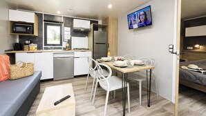Una kitchenette compacta con microondas, estufa y refrigerador. Una mesa de comedor con sillas está colocada en el centro, y un televisor está montado en la pared.