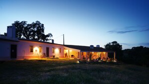 Una casa moderna con un porche cubierto y zona de estar al aire libre, rodeada de un campo cubierto de césped y árboles.