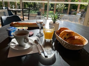 Une table avec des aliments pour le petit-déjeuner, notamment des croissants, une tasse de café, un verre de jus d’orange et une petite plante.