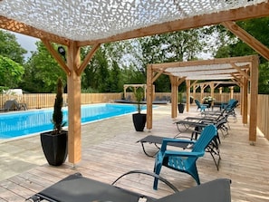 Une terrasse en bois avec des chaises longues et une piscine.