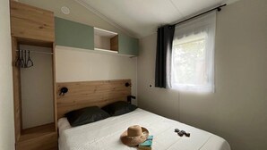A bedroom with a bed, a wardrobe, a window with curtains, and a small shelf above the bed.