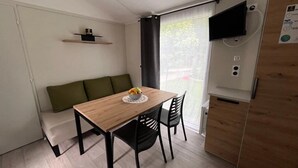 A compact living space with a wooden dining table, black chairs, a green sofa, and a TV mounted on the wall.