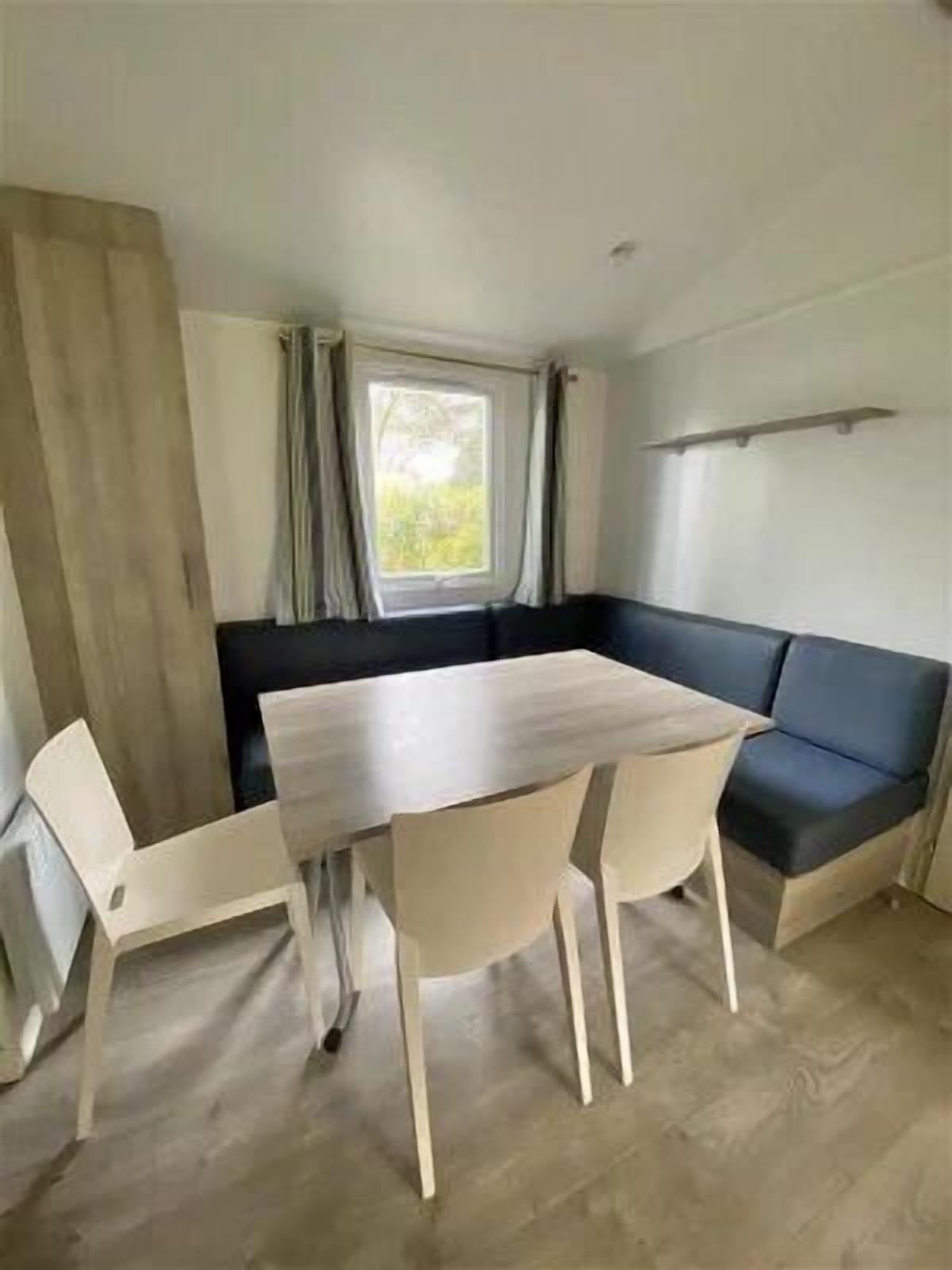 Una habitación pequeña con una mesa y sillas de madera, un sofá de color oscuro y una ventana con cortinas.