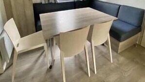 Ein kleiner Raum mit Holztisch und -stühlen, einem dunkelgrauen Sofa und einem Fenster mit Vorhängen.