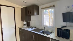 Una cocina compacta con armarios de madera oscura, un microondas integrado y una ventana con persianas.