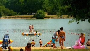 Escena a orillas de un lago con gente nadando y tomando el sol.