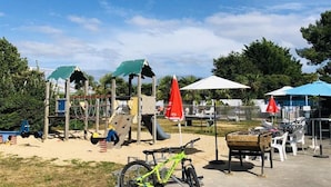 Un parque infantil con estructuras para escalar, una bicicleta y mobiliario exterior con sombrillas.