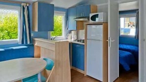 A compact kitchenette with a microwave, stove, and refrigerator. There is a small dining table with chairs and a window with curtains.