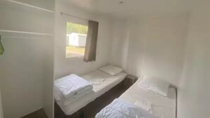 A small, sparsely furnished room with two single beds and a window. - ZEcamping 3 étoiles animé piscine chauffée locatif TV 27m2 4 pers (Guémené-Penfao)