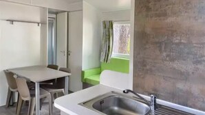A compact kitchen with a sink, a dining table with chairs, and a green cushioned bench. - ZEcamping 3 étoiles animé piscine chauffée locatif TV 27m2 4 pers (Guémené-Penfao)