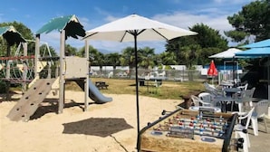 A playground with a slide and climbing structures, a foosball table, and outdoor seating under umbrellas.