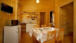 Ein Holzblockhaus-Interieur mit Küche, Esstisch, Stühlen, einem Fernseher und einer Mikrowelle.
