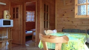 Ein Zimmer in einer Holzhütte mit einem Bett, einem Sessel, einer Mikrowelle und einem Fenster.
