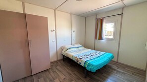 Un dormitorio con cama, armario, ventana con cortinas y puerta.