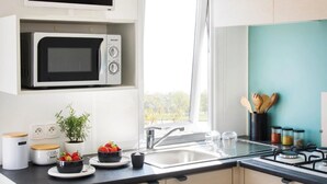 A modern kitchen with a built-in microwave, a sink, and a stove. There is a window providing natural light, and the kitchen features a teal backsplash.