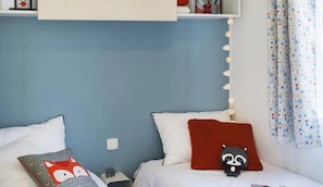 Un dormitorio con dos camas, una pared azul, un techo blanco y una ventana con cortinas estampadas.