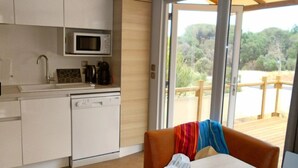 A modern kitchen with white appliances, a microwave, and a coffee maker. There is a view of a wooden deck and greenery outside.