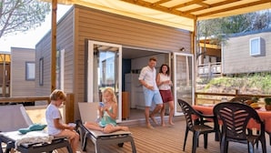 A wooden deck with a covered seating area, a small open-sided building, and a dining table with chairs.