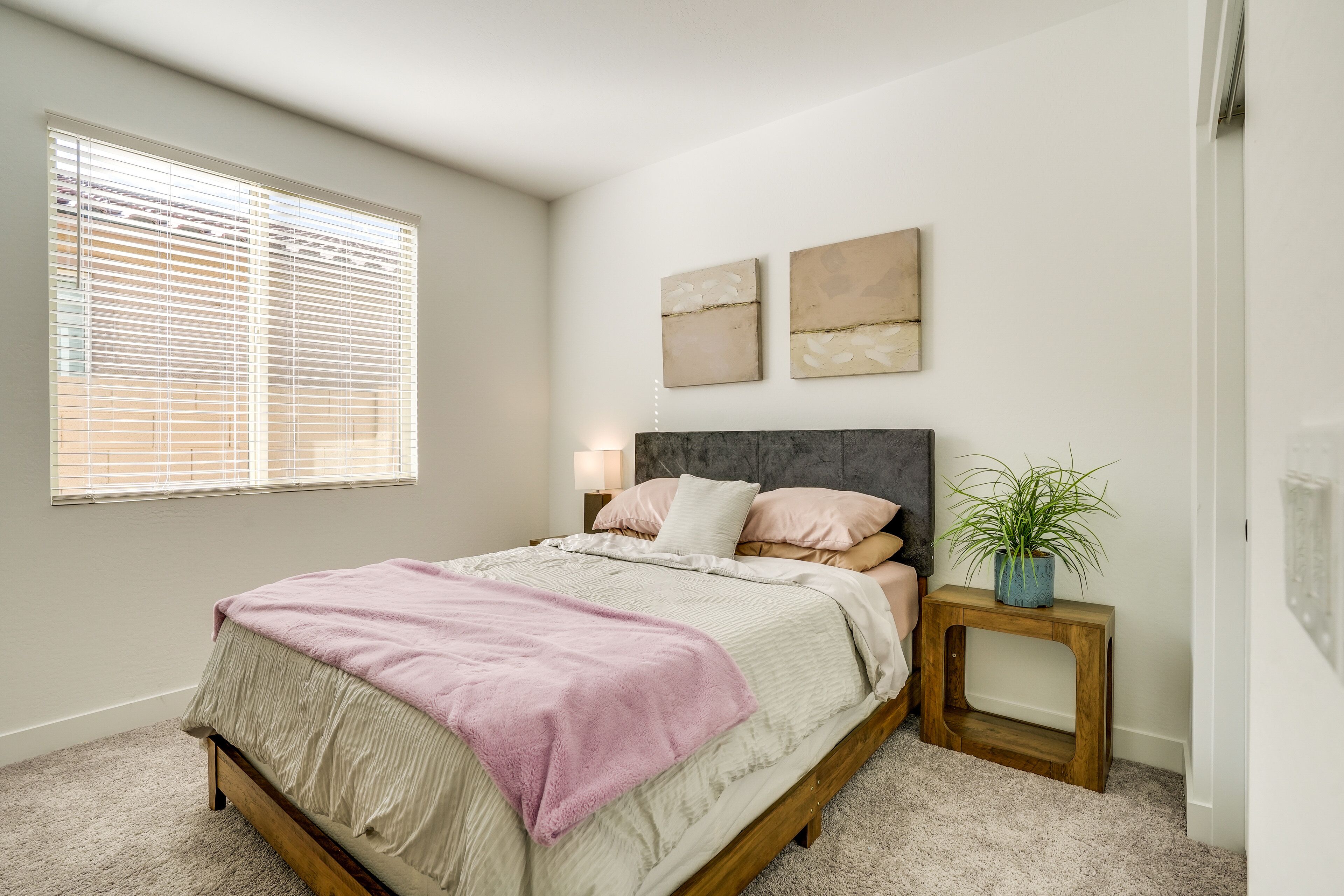 A bedroom with a bed, bedside tables, a window with blinds, and wall art.