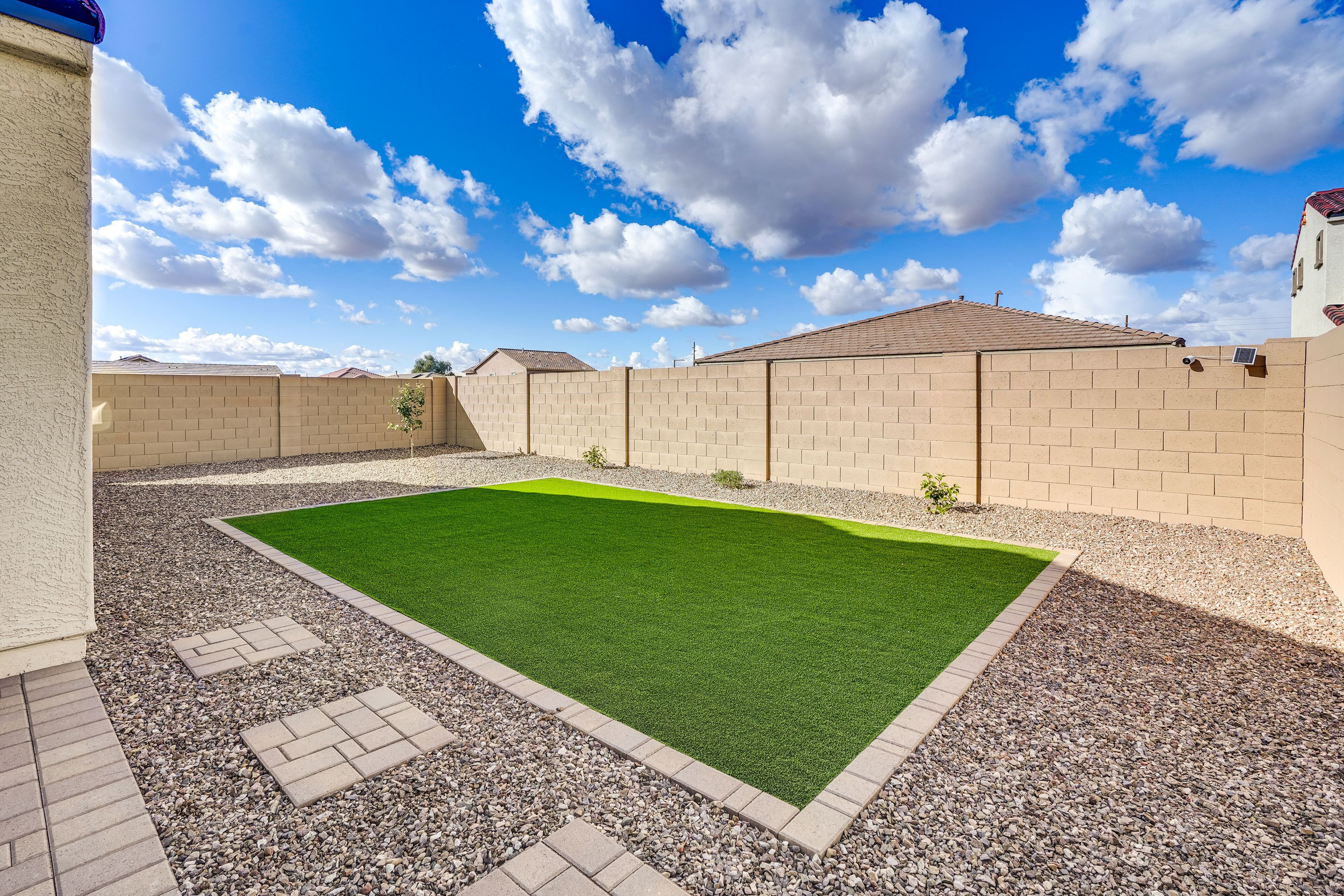 A backyard with a green lawn, a brick wall, and a clear blue sky.
