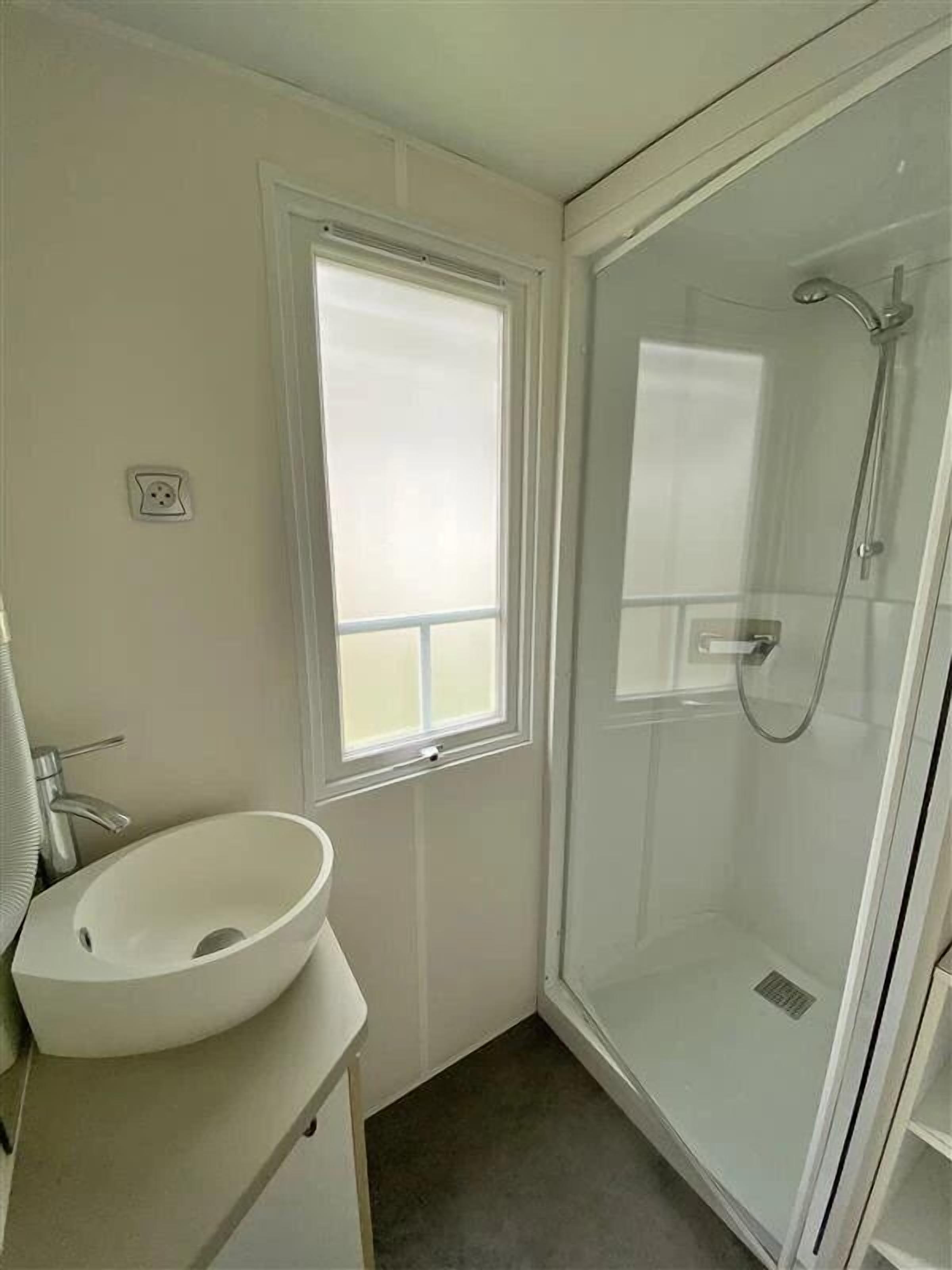 A bathroom with a white sink, a window, and a glass shower enclosure.