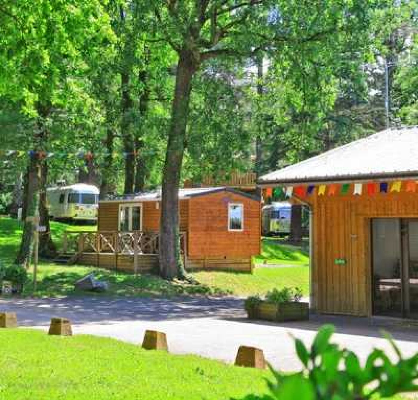 Eine Reihe aus Holzbungalows mit einem zentralen Gebäude, umgeben von Bäumen und einem gepflasterten Weg.