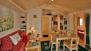 A cozy room with a wooden ceiling, a dining table with chairs, a red patterned sofa, and shelves with various items. - ZEcamping 4* familial espace aquatique chiens acceptés locatif LV BBQ (Albi)