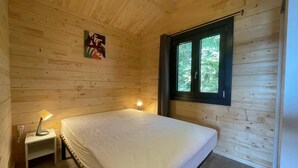 A wooden cabin room with a bed, a small bedside table, a window, and a painting on the wall.