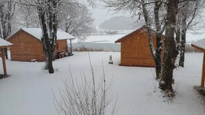 A snow-covered outdoor area with wooden cabins, a small pond, and bare trees.