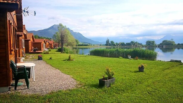 A lakeside lodge with outdoor seating, a gravel path, and a view of mountains.