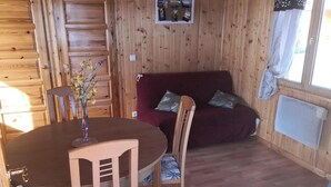A wooden cabin interior with a dining table, chairs, a sofa, and a picture on the wall.