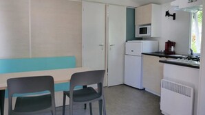 Eine kompakte Küchenzeile mit Mikrowelle, kleinem Kühlschrank und Herd. Ein Essbereich mit Tisch und zwei Stühlen ist ebenfalls vorhanden.