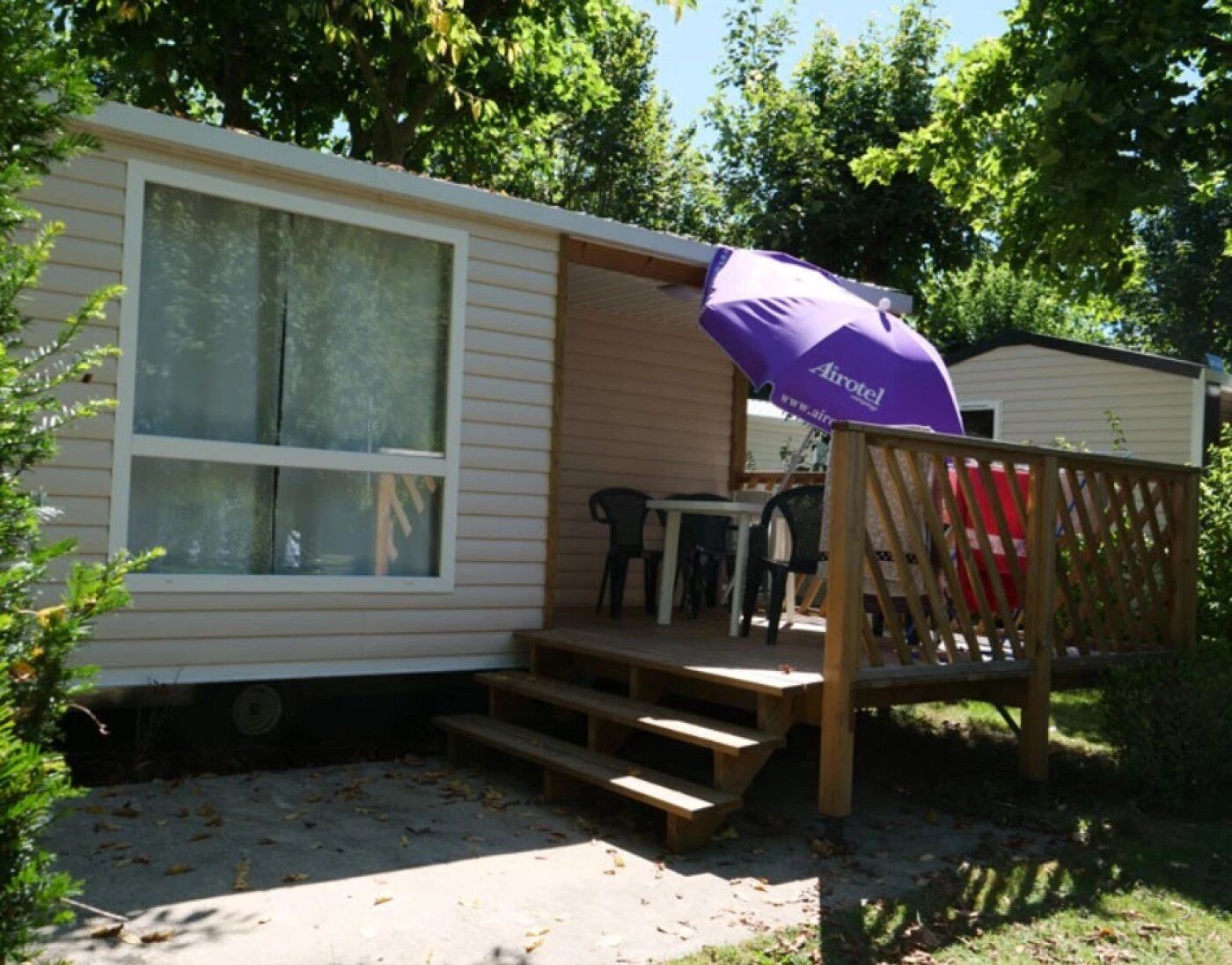 A mobile home with a covered patio area, a wooden deck, and a purple Airotel umbrella.