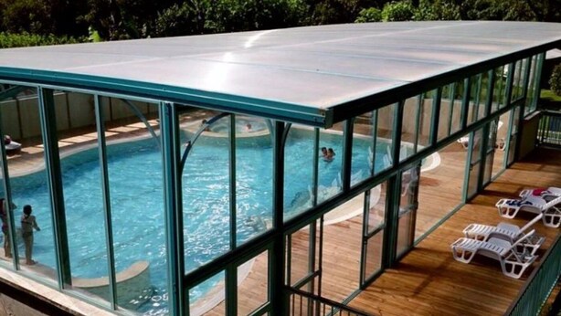 Une piscine intérieure entourée de parois en verre, avec une terrasse en bois et des chaises longues.