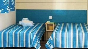 A room with two single beds with striped bedding, a shelf with various items, and a blue curtain. - ZEcamping 4 étoiles piscine couverte cottage 31m2 (Argentat)