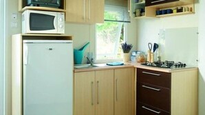 A compact kitchen with a refrigerator, microwave, stove, and wooden cabinets. - ZEcamping 4 étoiles piscine couverte cottage 31m2 (Argentat)