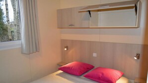 Um quarto com cama beliche, duas almofadas cor-de-rosa, uma mesa de cabeceira, um espelho e uma janela com cortinas.