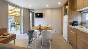 A modern kitchen with a dining area, wooden cabinets, a TV, and a view to the outside.